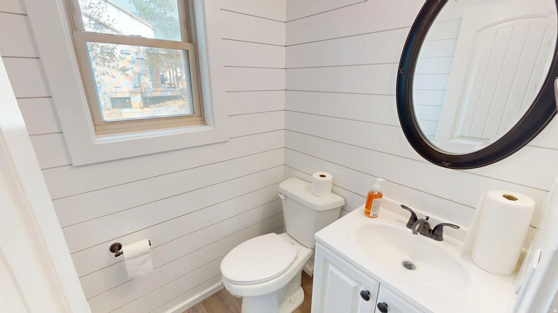 Bathroom featuring horizontal white shiplap wall paneling, a single-pane window with wood-finish trim, and a white vanity with a dark oval mirror