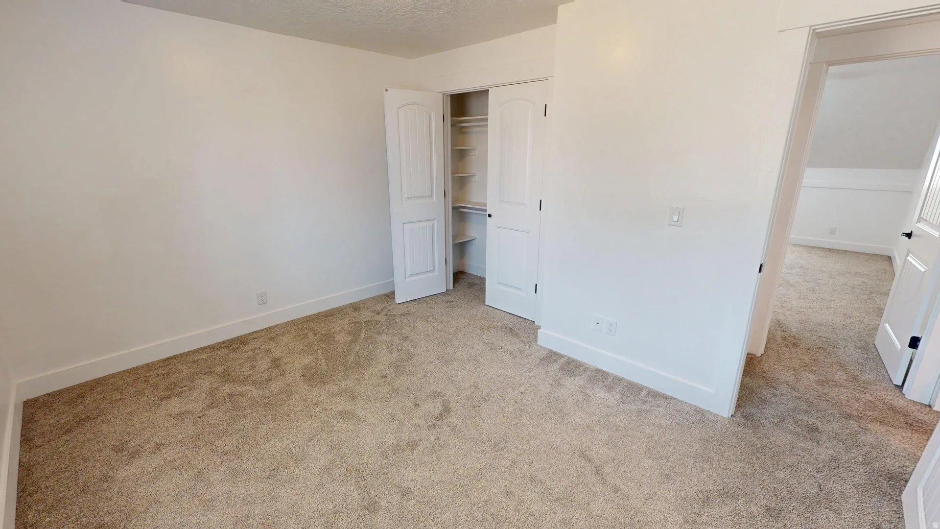 Carpeted room with white walls, white baseboards, and a bi-fold closet door featuring shelving