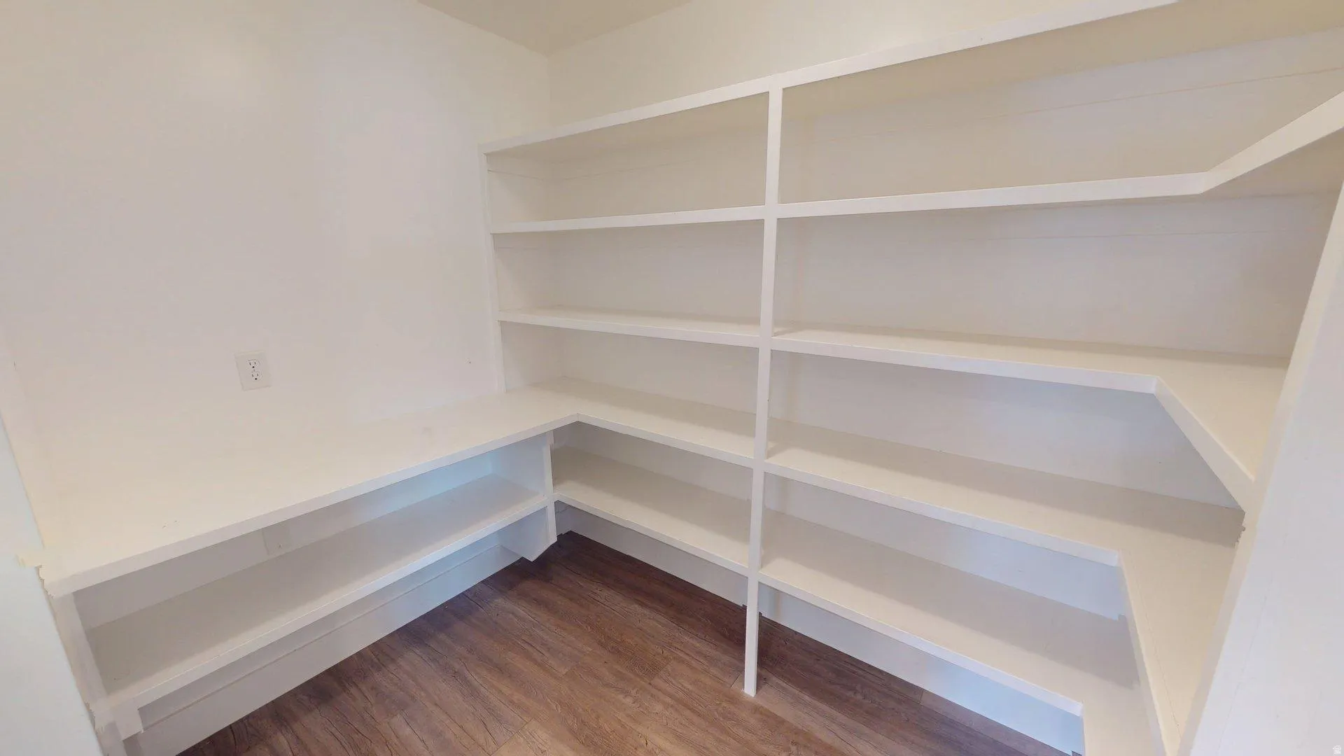 Pantry featuring extensive built-in white shelving, wood-finish flooring, and a corner configuration