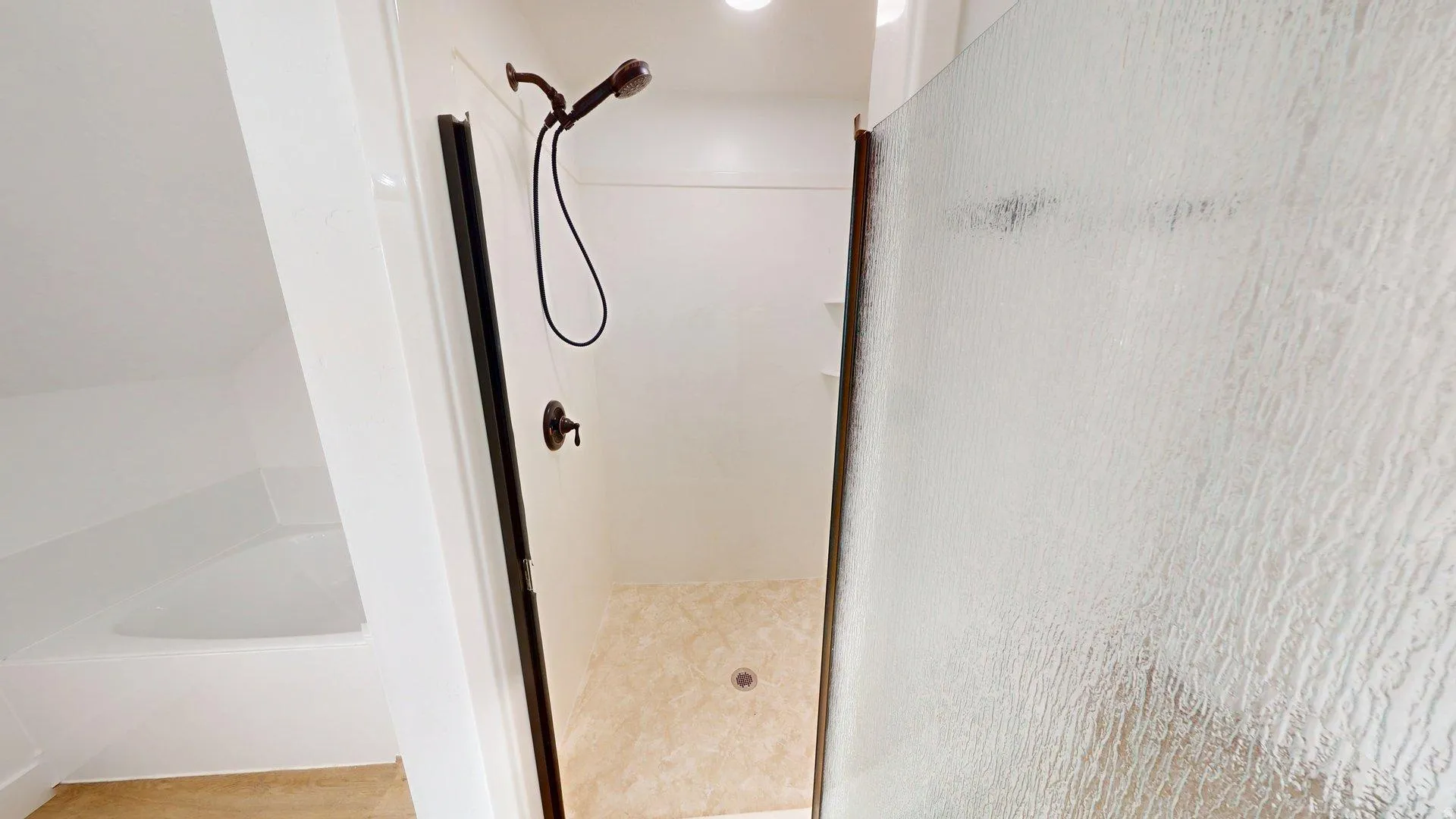 Shower with a bronze-toned fixture, textured glass shower door, and a light-toned patterned shower floor