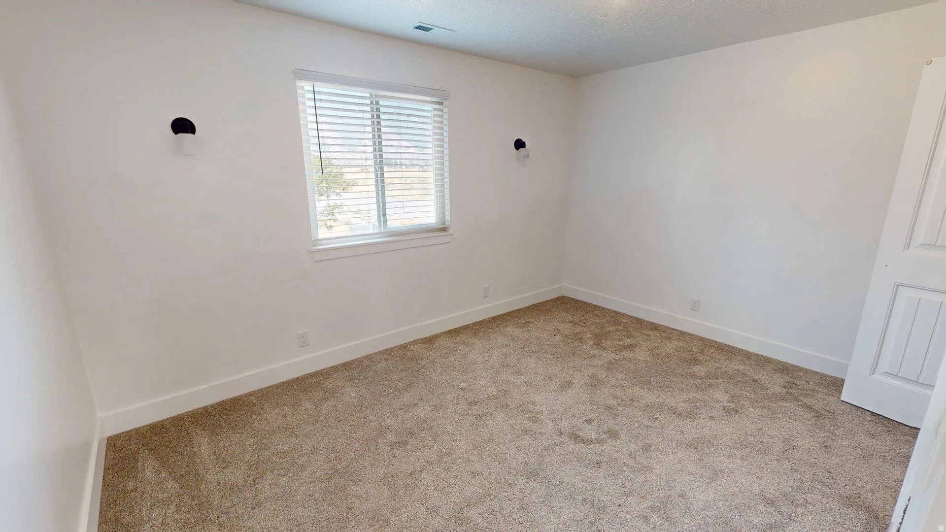 Carpeted room with a prominent window featuring horizontal blinds