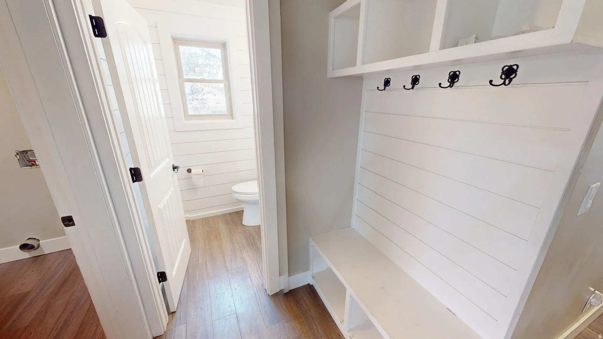 Built-in mudroom bench with storage cubbies and upper shelving, featuring shiplap-style paneling and five decorative hooks