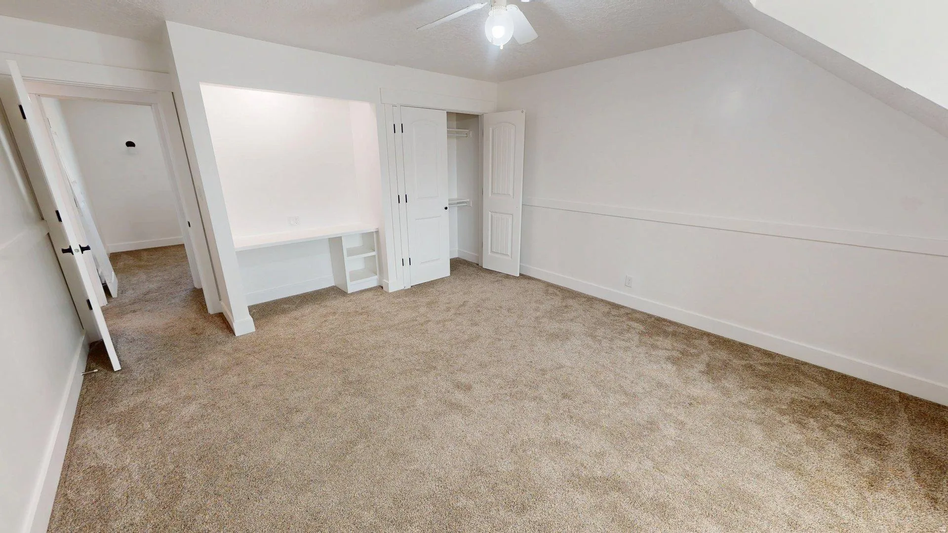 Carpeted room with white walls, a built-in desk with shelving, and a white bi-fold closet door