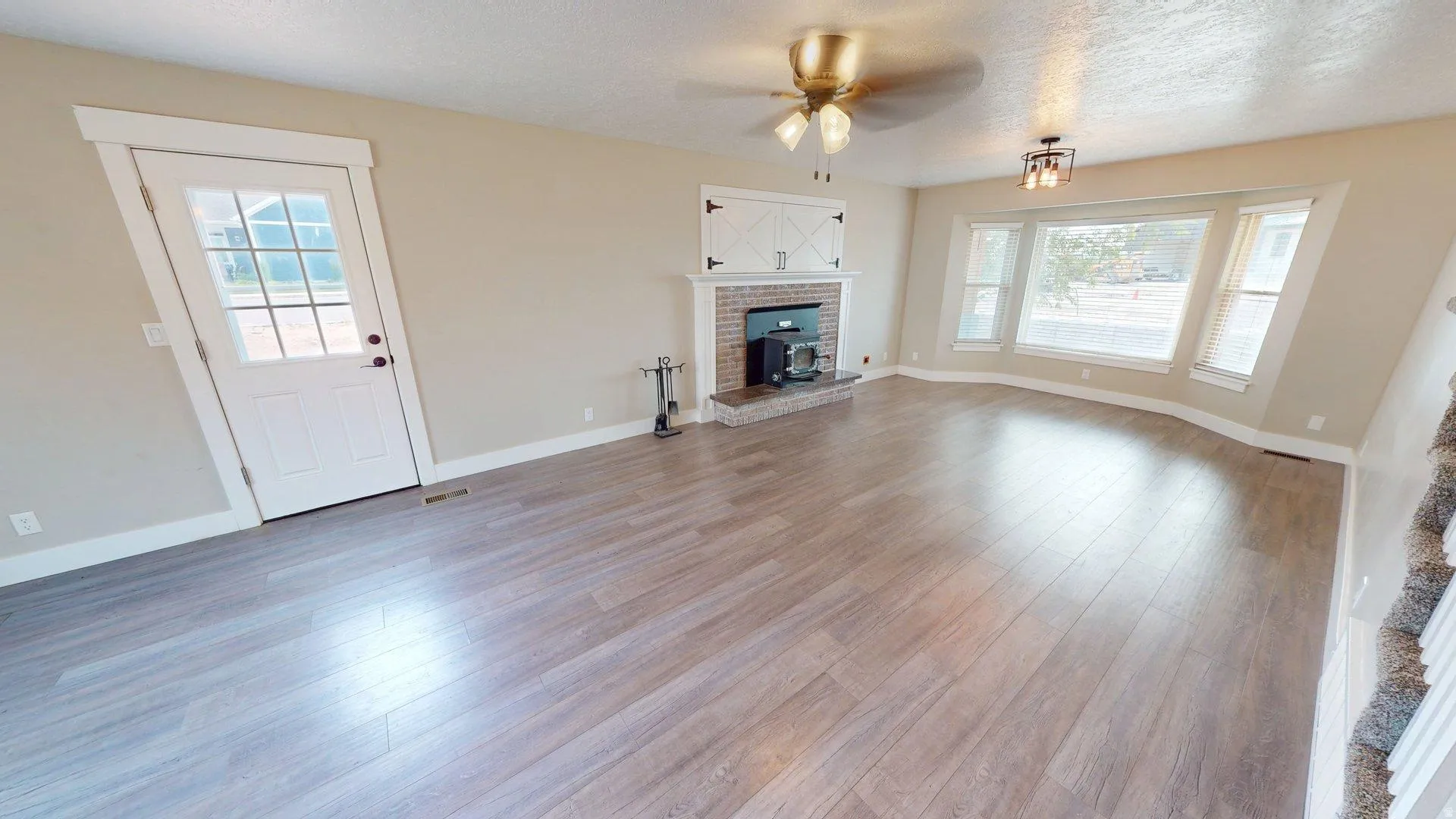 Spacious living area featuring wood-finish flooring, a brick fireplace with a decorative mantel, and a bay window