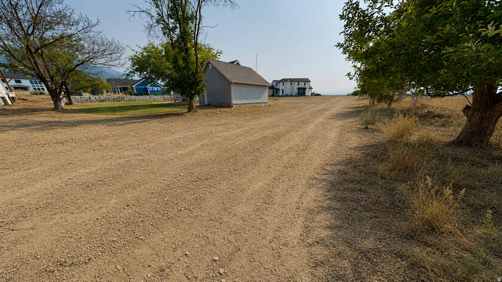 Ai enhanced photo. Expansive gravel driveway with a detached accessory building, mature trees, and distant mountain range