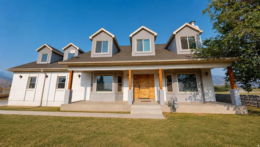 Ai enhanced photo. Contemporary home with a blend of white brick and gray stucco siding, featuring multiple dormer windows, a covered front porch with wood-wrapped columns, and a wide concrete walkway