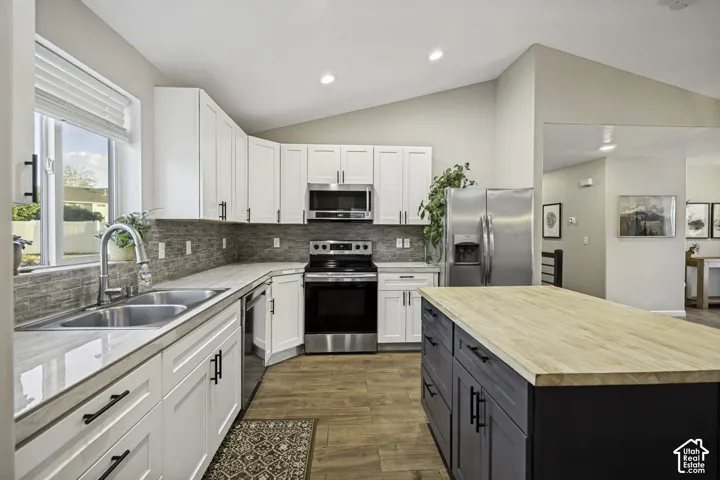 Kitchen featuring white upper and lower cabinetry, stainless steel appliances, a stacked stone backsplash, and wood-finish flooring