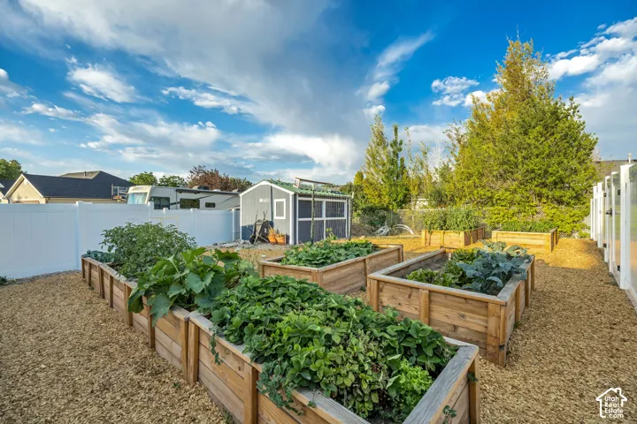 Backyard featuring multiple raised garden beds, gravel pathways, a white vinyl privacy fence, a detached shed, and mature trees