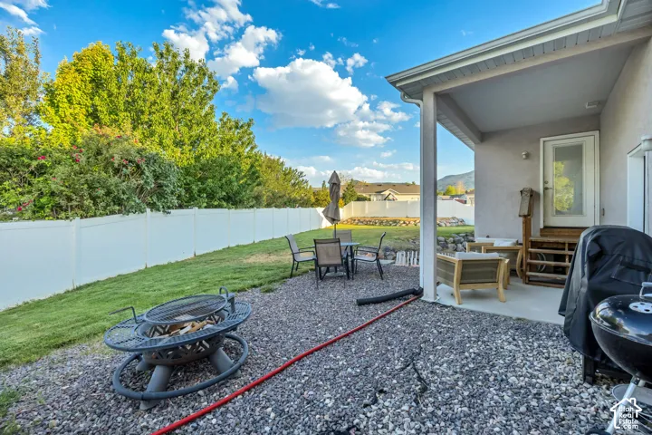Expansive backyard featuring a covered concrete patio, gravel hardscaping, a fire pit, and a white privacy fence