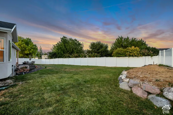 Expansive backyard featuring a lush lawn, white privacy fencing, and a built-in stone retaining wall