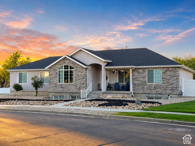 Ranch-style residence featuring a stucco and stone veneer facade, a dark shingle roof, and an inviting front porch
