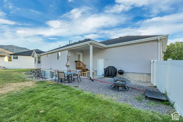 Rear exterior featuring a covered patio with a gravel surface, a grassy lawn area, and a white privacy fence