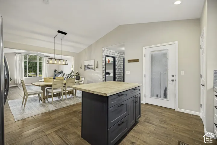 Open-concept kitchen and dining area featuring wood-finish flooring, a kitchen island with dark cabinetry and a light-toned countertop, and vaulted ceilings