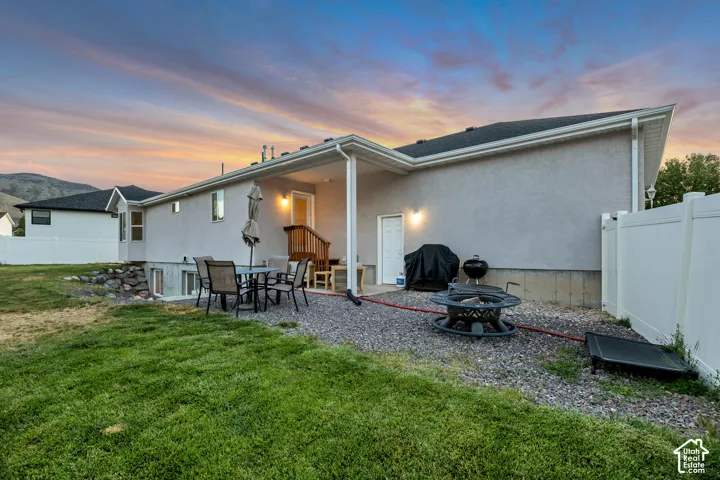 Rear exterior featuring a covered patio with a gravel seating area, a private yard with partial fencing, and a mountain backdrop