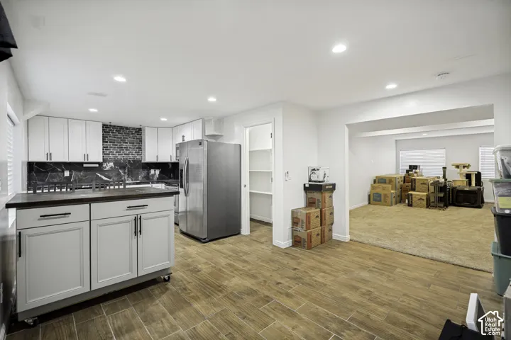 Modern kitchen featuring wood-finish flooring, white cabinetry with black hardware, black marble-patterned backsplash, and stainless steel appliances