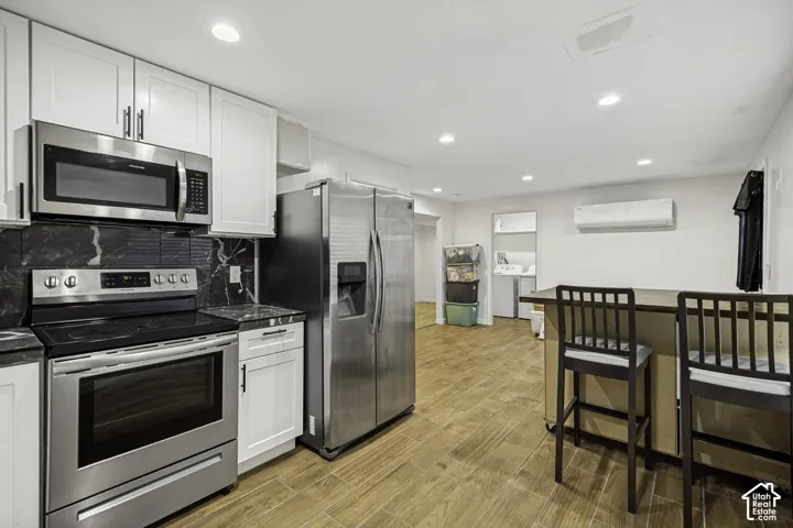Modern kitchen featuring stainless steel appliances, white cabinetry, dark stone countertops, and a complementary black tile backsplash