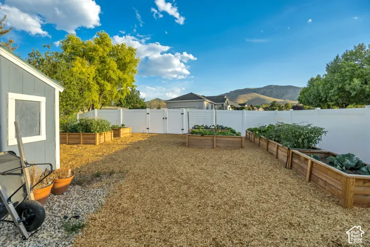 Backyard area featuring multiple wooden raised garden beds, a white vinyl fence, and a gray storage shed with a window