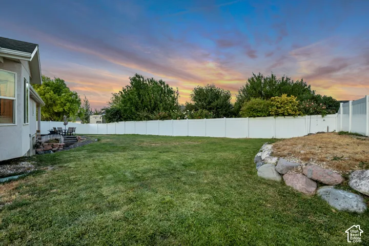 Spacious backyard featuring a large grass lawn, white privacy fencing, and a stone retaining wall
