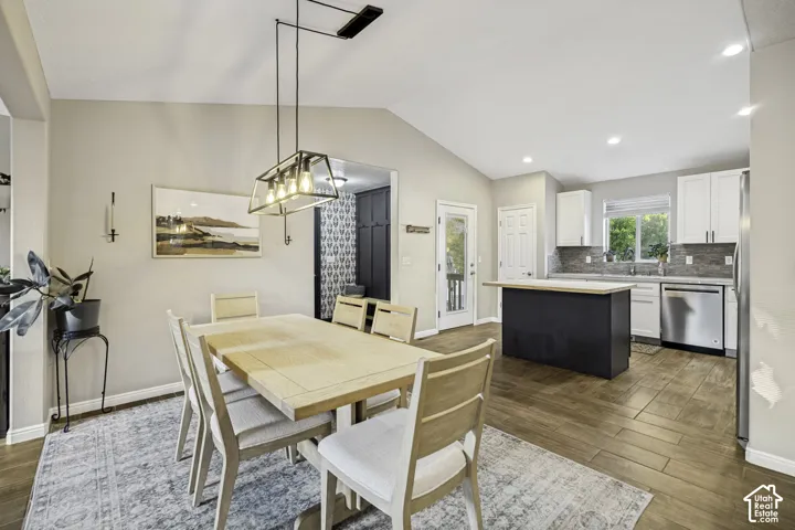 Vaulted ceiling dining area featuring wood-finish flooring, a contemporary linear chandelier, and access to the kitchen