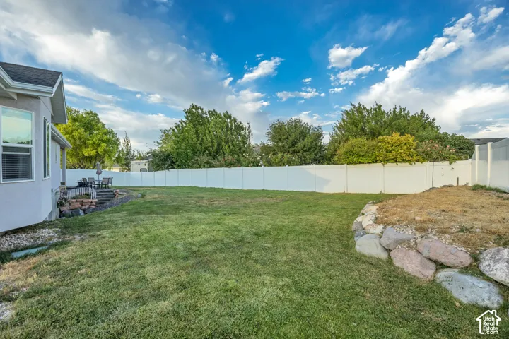 Expansive backyard featuring a large green lawn, full privacy fencing, a multi-level patio, and a natural stone retaining wall