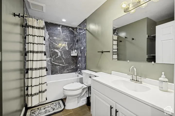 Bathroom featuring a shower-tub combination with dark marble-style surround, white vanity with integrated sink, chrome faucet, and wood-finish flooring