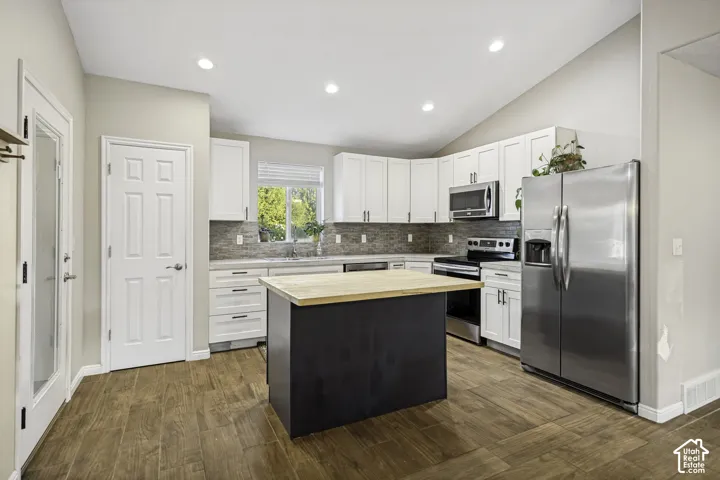 Modern kitchen featuring white cabinetry, stainless steel appliances, a center island with a wood-finish countertop, wood-finish flooring, and a tiled backsplash