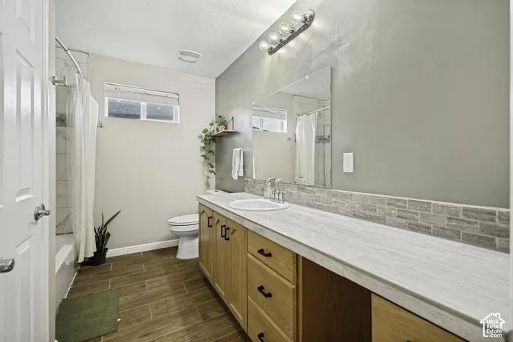 Bathroom with a wood-finish tile floor, an extended vanity featuring light wood-finish cabinetry, a white countertop, and a tiled backsplash