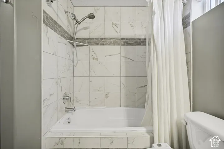 Bathtub and shower combination featuring white large-format wall tiles with subtle veining, a decorative mosaic tile accent band, and chrome fixtures including a handheld showerhead