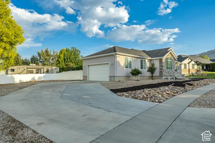 Contemporary ranch-style residence featuring a split-level driveway, attached garage, stone facade accents, and a sidewalk