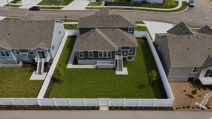 Expansive backyard featuring a manicured lawn, white privacy fencing, and mature trees