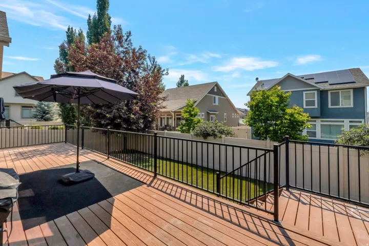 Spacious outdoor deck featuring wood-finish flooring, black metal railings, and a fenced backyard with a manicured lawn