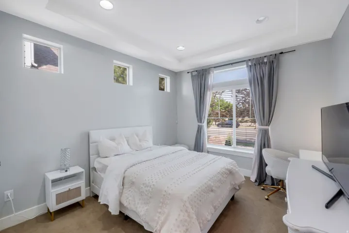 Recessed lighting illuminates this room featuring light gray walls and a tray ceiling