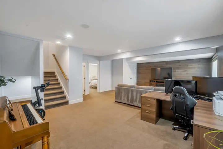Spacious basement room featuring carpet flooring, recessed lighting, a wooden accent wall, and a built-in entertainment console