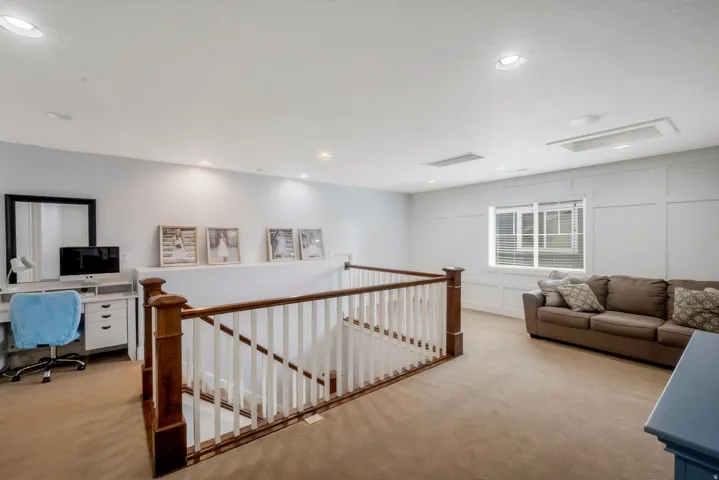 Carpeted upper-level landing featuring a wood-finish railing, recessed lighting, and a large window with blinds
