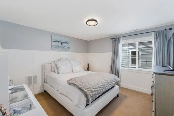 Bedroom featuring wainscoting, light gray walls, and a window with blinds and drapes