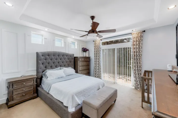 Spacious room featuring ceiling fan, recessed lighting, tray ceiling, sliding glass doors with vertical blinds, and upper transom windows