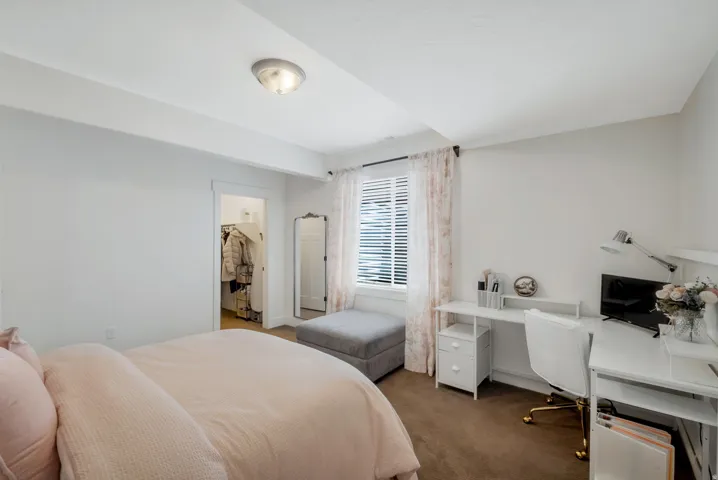 Neutral-toned bedroom featuring a compact closet with a built-in shelving system, a window with horizontal blinds, and a flush-mount ceiling light fixture