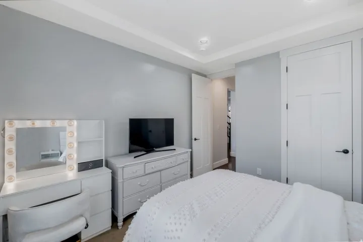 Recessed lighting illuminates a room featuring light gray walls, a tray ceiling, and white three-panel interior doors with matte black hardware