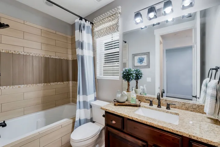 Bathroom featuring a built-in tub with tile surround, a dark wood-finish vanity with a light-toned granite countertop, an undermount sink, and a multi-bulb vanity light fixture