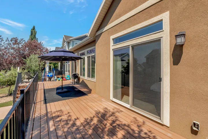 Expansive wood-finish deck with black metal railings, a stucco exterior, multiple windows, and a sliding glass door
