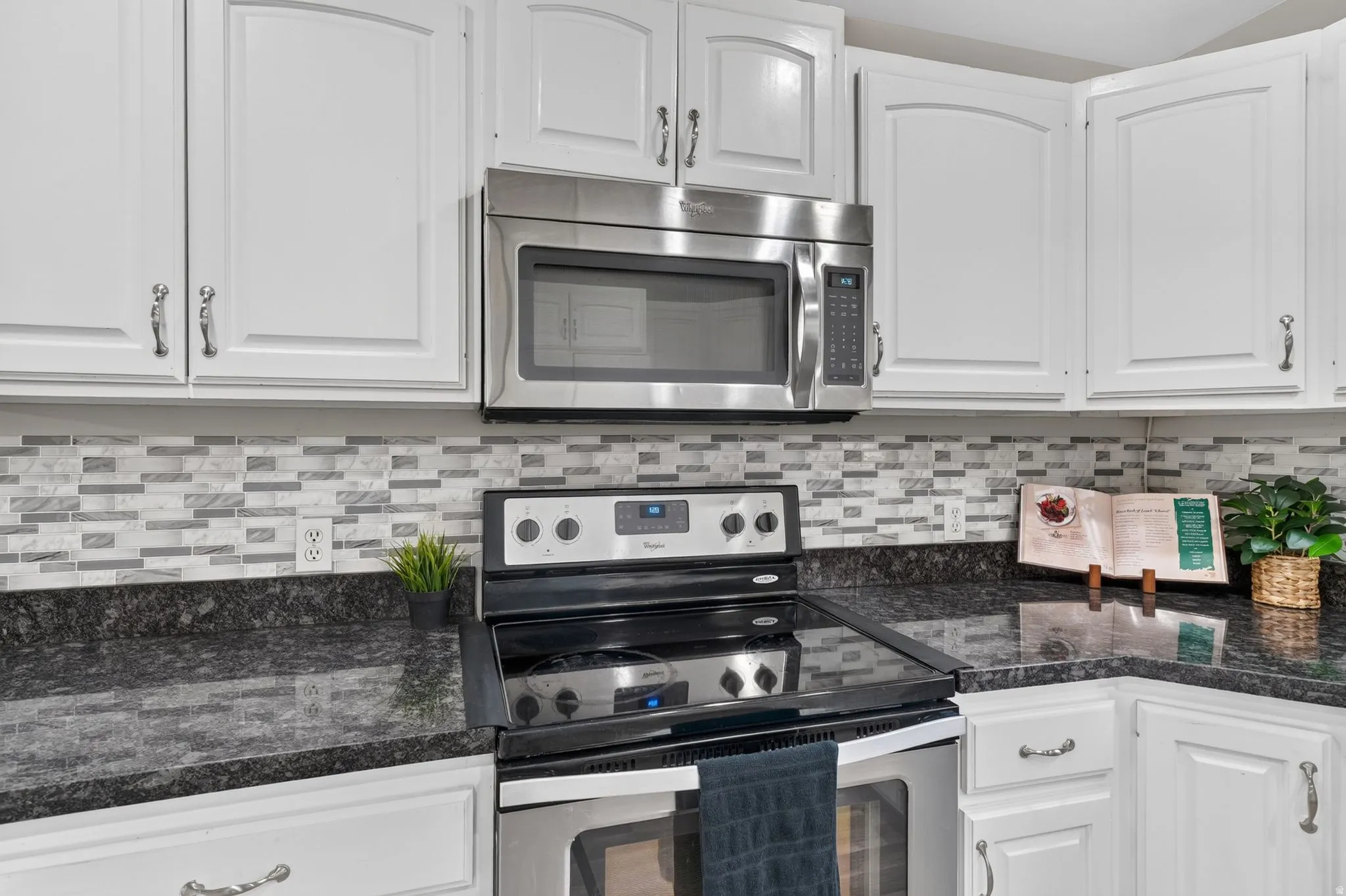 Kitchen featuring white cabinetry, a stainless steel over-the-range microwave, a black electric range, dark countertops, and a mosaic tile backsplash