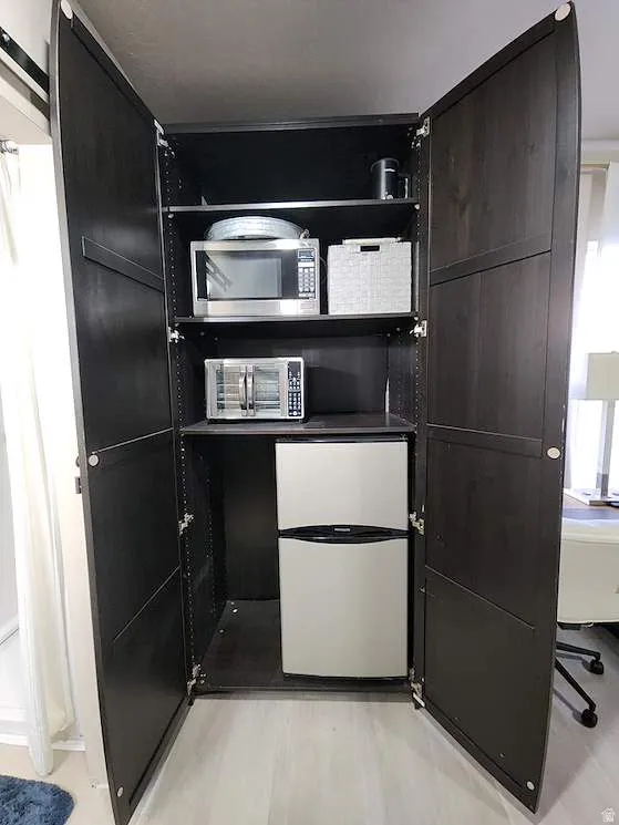 Integrated kitchenette featuring dark wood-finish cabinetry, adjustable shelving, and a compact stainless steel refrigerator