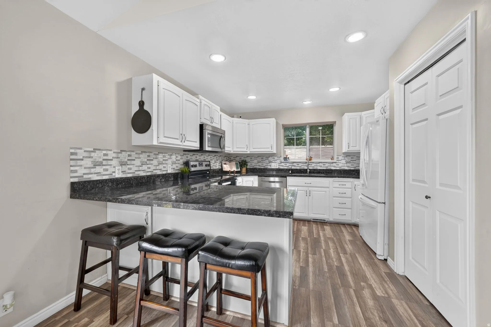 Kitchen featuring wood-finish flooring, white cabinetry, a dark countertop, a mosaic tile backsplash, and recessed lighting