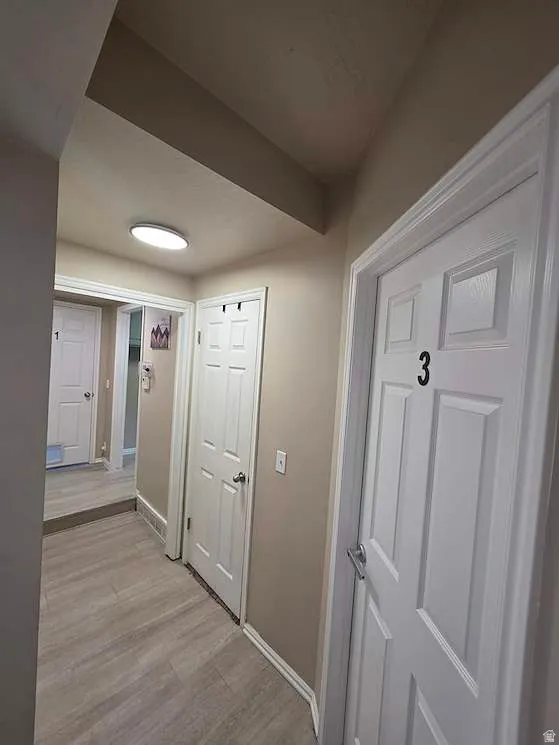 Hallway featuring wood-finish flooring, light tan wall paint, and white trim