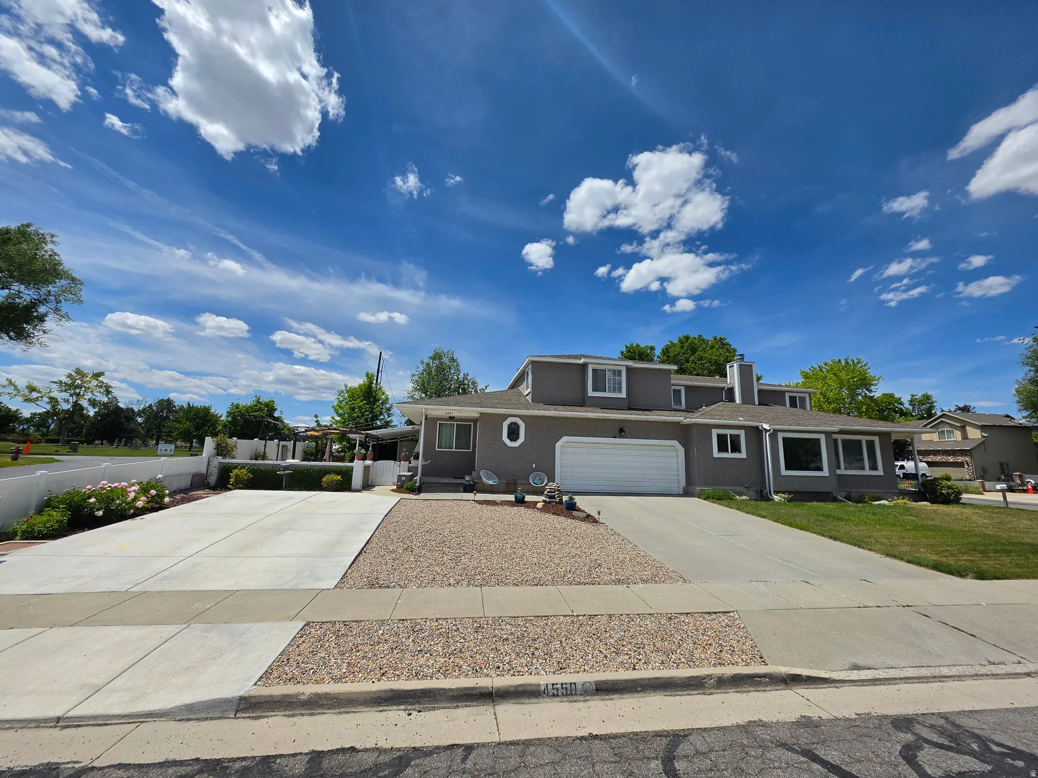 Front exterior featuring a gray stucco finish, white trim windows, a white garage door, and a concrete driveway