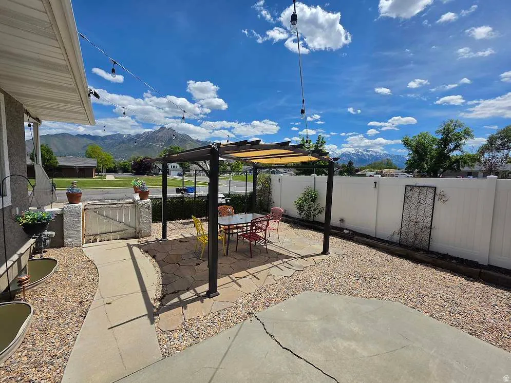 Outdoor entertaining area featuring a stone patio, a dark-framed pergola with a light-colored retractable canopy, and gravel landscaping