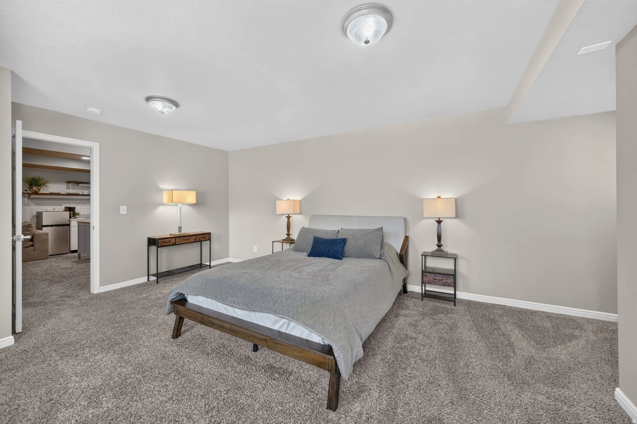 Spacious carpeted room featuring a neutral color palette, recessed ceiling light fixtures, and a doorway opening to an additional living space with built-in shelving