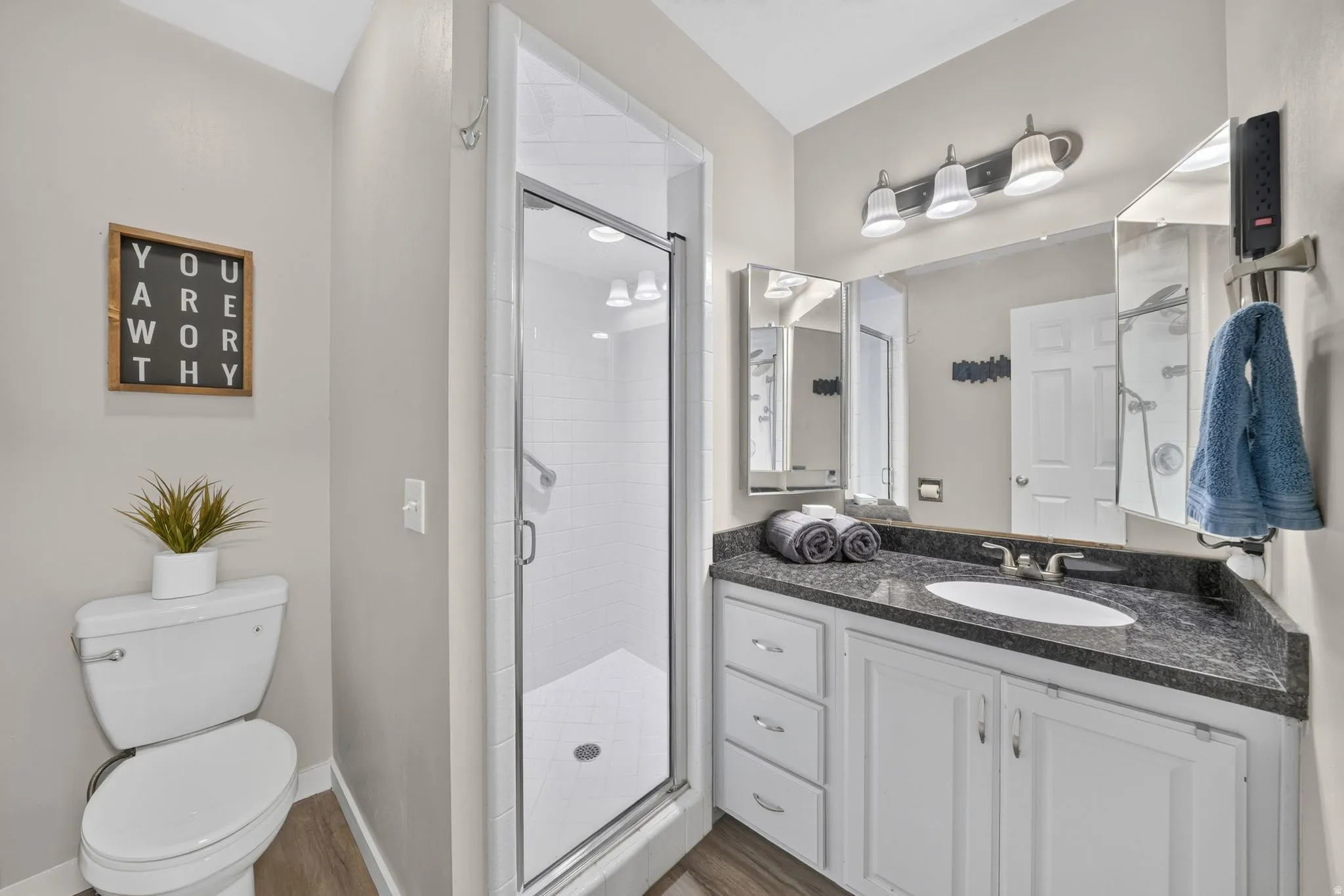 Modern bathroom featuring a glass-enclosed shower with subway tile, a vanity with a dark speckled countertop, white cabinetry, and wood-finish flooring