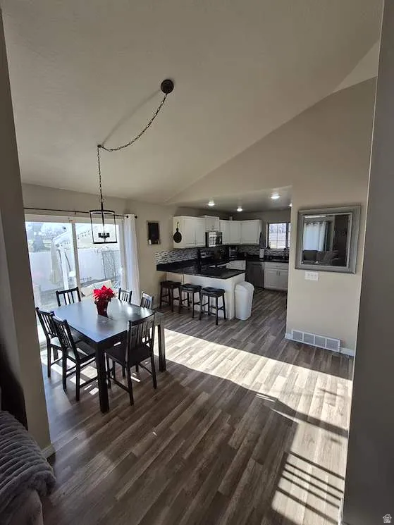 Open-concept living area featuring wood-finish flooring, a dining space with a contemporary hanging light fixture, and a kitchen with an island breakfast bar and white cabinetry
