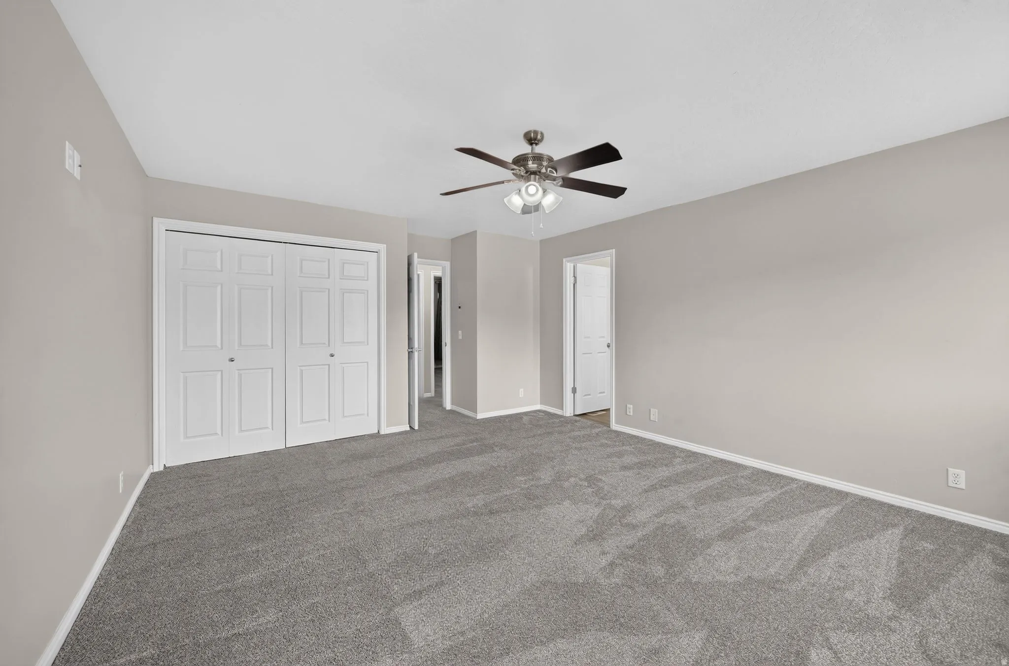 Spacious room featuring neutral paint, gray carpeting, a ceiling fan with integrated lighting, and bi-fold closet doors